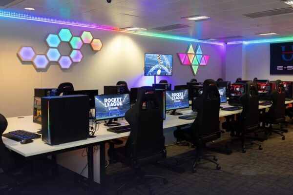 Moderne esports-gamingruimte met rijen computers en ergonomische stoelen, sfeervol verlicht met RGB-lampen en hexagonale wandpanelen.
