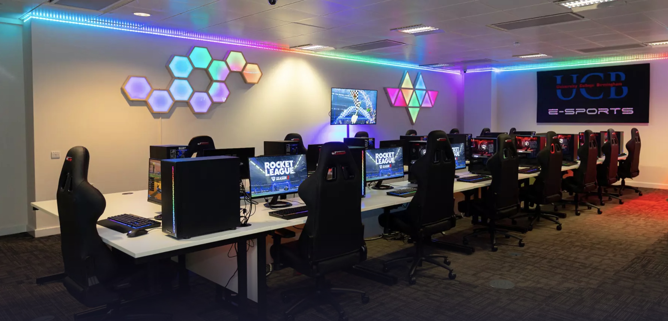 Moderne esports-gamingruimte met rijen computers en ergonomische stoelen, sfeervol verlicht met RGB-lampen en hexagonale wandpanelen.