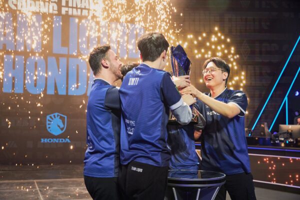 Esports-team in blauwe jerseys viert overwinning op het podium met trofee en confetti tijdens een levendig kampioenschapsevenement.