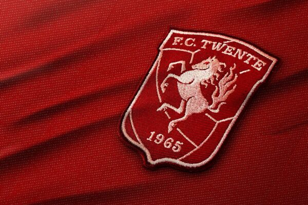 Het logo van FC Twente, een Nederlandse voetbalclub uit Enschede, geborduurd op een rode stof. Het logo toont een steigerend paard, een symbool van kracht en vastberadenheid, met het jaartal 1965 onder het paard. Dit jaar markeert de oprichting van de club.