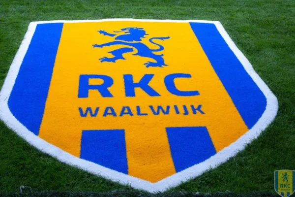 Het logo van RKC Waalwijk op het voetbalveld, een blauw en geel embleem met een staande leeuw en de naam van de club.