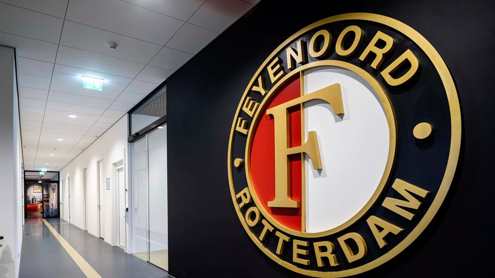 Het logo van Feyenoord Rotterdam aan de muur van het stadion, met de iconische gouden "F" in het midden, omgeven door de clubkleuren rood, wit en zwart.