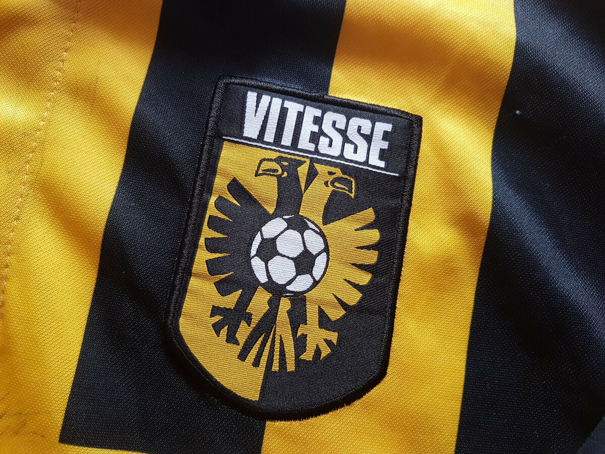 Op het embleem staat de clubnaam “Vitesse” in vette letters boven een gestileerde zwarte adelaar die een voetbal vasthoudt, tegen de traditionele geel met zwart gestreepte achtergrond.