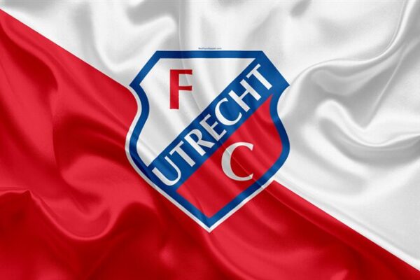 Het logo van FC Utrecht is prominent weergegeven op een zijdezachte rode en witte achtergrond, symboliserend de clubkleuren. Het herkenbare embleem toont een rood 'F' en 'C' tegen een witte achtergrond, met een blauwe omranding waarin 'Utrecht' staat geschreven.